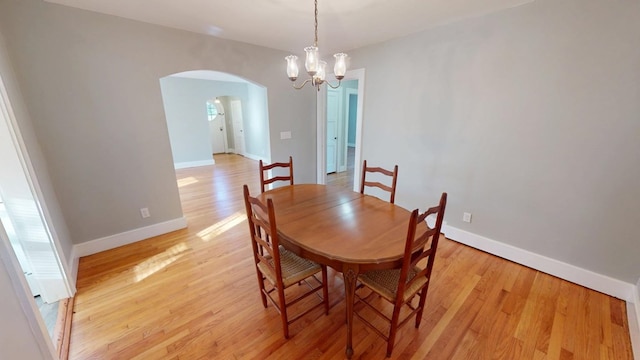 dining room with light wood-style floors, arched walkways, baseboards, and an inviting chandelier