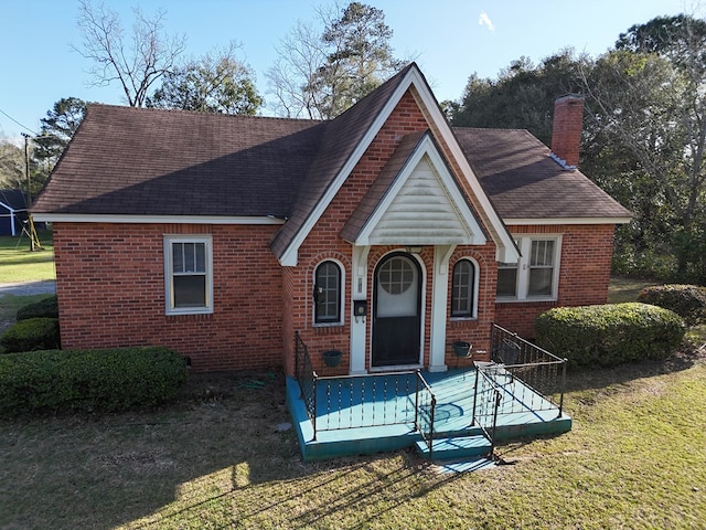 tudor home with roof with shingles, a front yard, a chimney, and brick siding