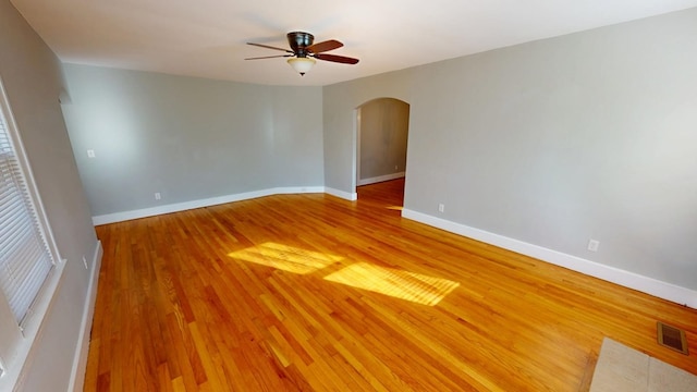 empty room with arched walkways, visible vents, light wood-style flooring, and baseboards