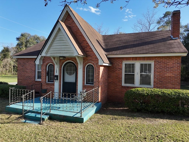 view of front of house featuring a chimney, a front lawn, and brick siding