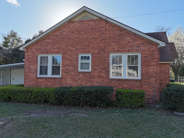 view of side of home with roof with shingles, brick siding, and a lawn