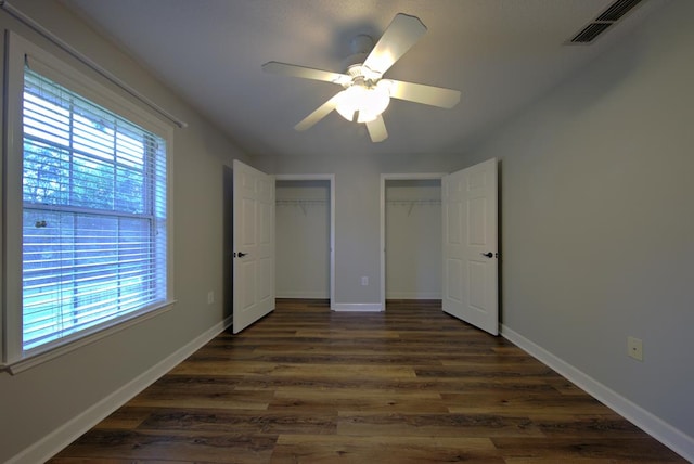 unfurnished bedroom featuring multiple closets, dark wood-type flooring, visible vents, and multiple windows