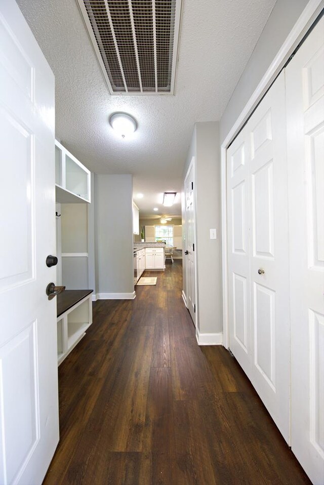 hall featuring a textured ceiling, baseboards, dark wood-style floors, and visible vents