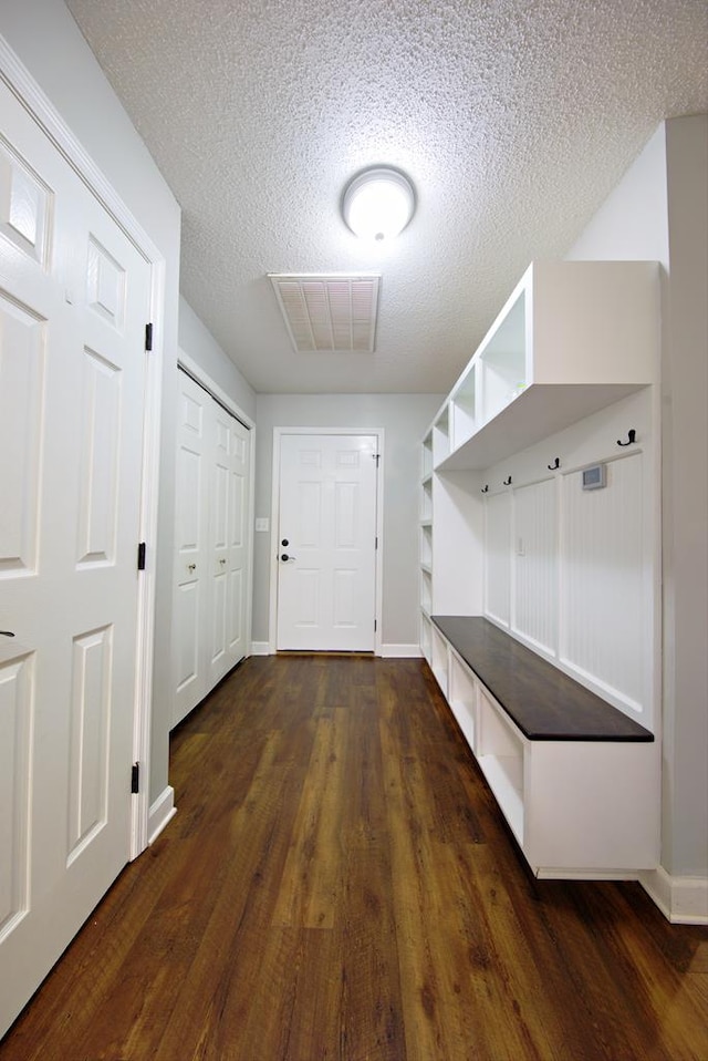 mudroom featuring a textured ceiling, visible vents, baseboards, and dark wood-style floors