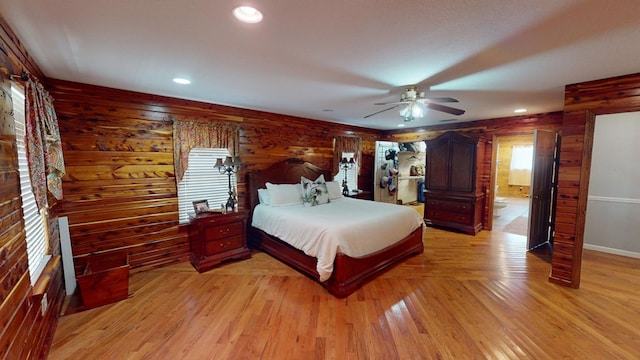 bedroom featuring ensuite bathroom, wood walls, ceiling fan, and light hardwood / wood-style flooring