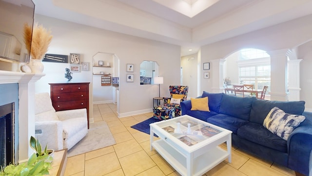 living room featuring crown molding, a tray ceiling, decorative columns, and light tile patterned floors