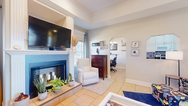 living room with crown molding, a raised ceiling, a tile fireplace, and light tile patterned floors