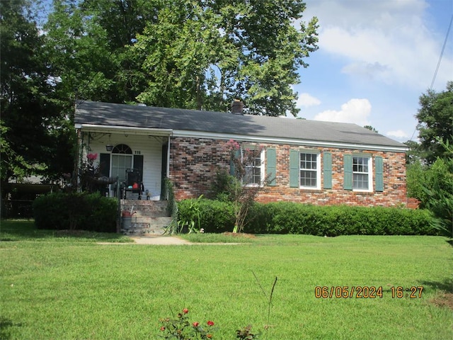 view of front facade featuring a front yard, a porch, a chimney, and brick siding