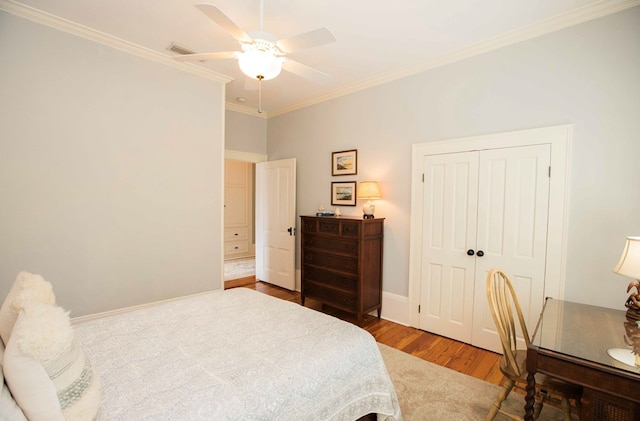 bedroom with wood-type flooring, ceiling fan, crown molding, and a closet