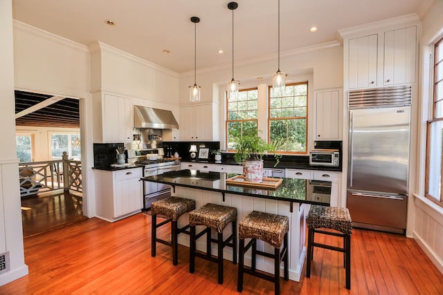 kitchen featuring white cabinetry, appliances with stainless steel finishes, a breakfast bar area, and wall chimney range hood