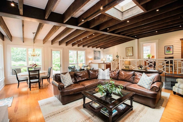 living room with an inviting chandelier, vaulted ceiling with skylight, light hardwood / wood-style flooring, and a wealth of natural light