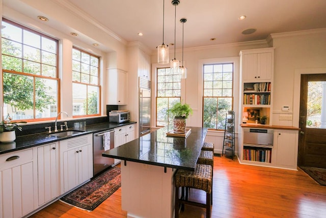 kitchen featuring sink, appliances with stainless steel finishes, white cabinetry, hanging light fixtures, and a kitchen island