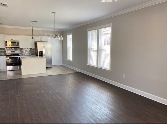 kitchen featuring pendant lighting, stainless steel appliances, tasteful backsplash, ornamental molding, and white cabinets