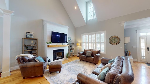 living room with decorative columns, high vaulted ceiling, and light hardwood / wood-style flooring