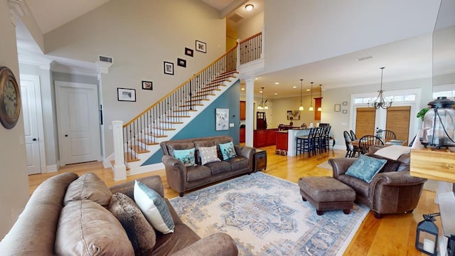 living room featuring a notable chandelier, crown molding, light hardwood / wood-style floors, and a high ceiling