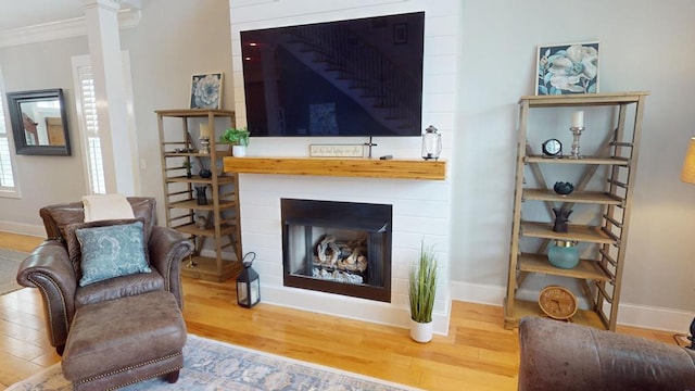 sitting room featuring hardwood / wood-style flooring, a large fireplace, crown molding, and ornate columns