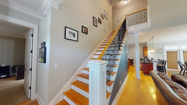 stairway with crown molding, decorative columns, a high ceiling, and hardwood / wood-style flooring