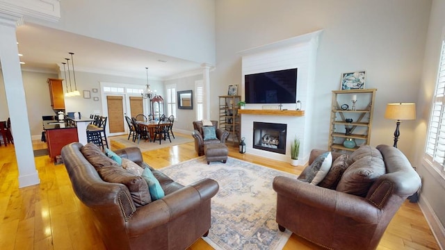 living room with a notable chandelier, crown molding, light hardwood / wood-style flooring, and decorative columns