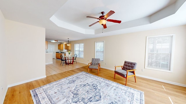 living area with ceiling fan, a tray ceiling, and light hardwood / wood-style floors