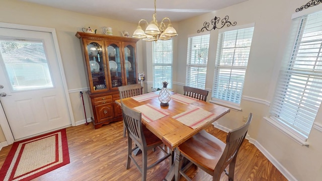 dining space featuring light wood-style flooring, baseboards, and a notable chandelier