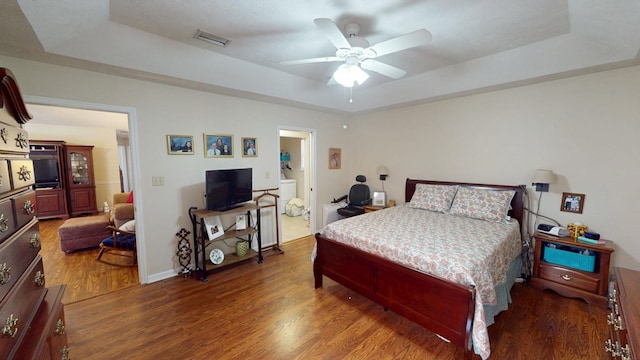 bedroom with ceiling fan, a tray ceiling, wood finished floors, and visible vents