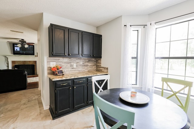 351 Plantation Ln, Thomasville, GA 31757 - kitchen featuring ceiling fan, a textured ceiling, decorative backsplash, dark cabinets, and a fireplace