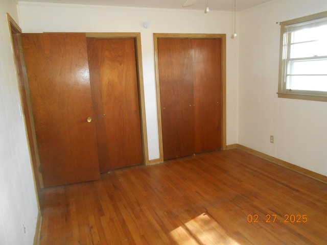 unfurnished bedroom with crown molding, two closets, baseboards, and wood finished floors