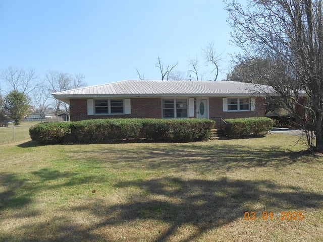 ranch-style home featuring a front yard, metal roof, brick siding, and fence