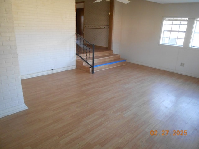 spare room featuring stairs, ceiling fan, brick wall, and wood finished floors