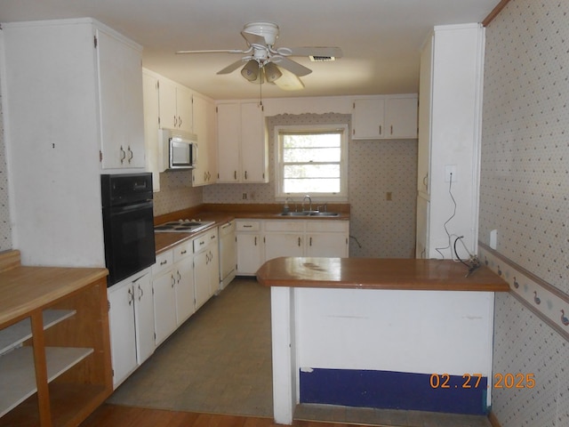 kitchen featuring a sink, white cabinets, black oven, dishwasher, and wallpapered walls