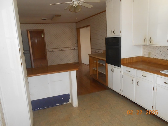 kitchen with wall oven, wallpapered walls, white cabinets, a ceiling fan, and ornamental molding