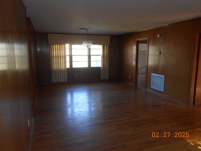 unfurnished room with wooden walls, wood finished floors, visible vents, and an inviting chandelier