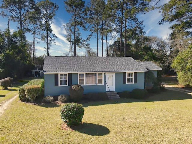 single story home with entry steps, roof with shingles, a front yard, and stucco siding