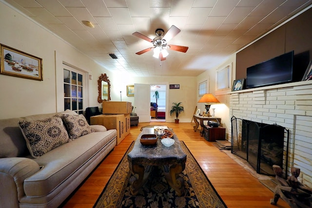 living area with light wood finished floors, a fireplace, visible vents, and a ceiling fan