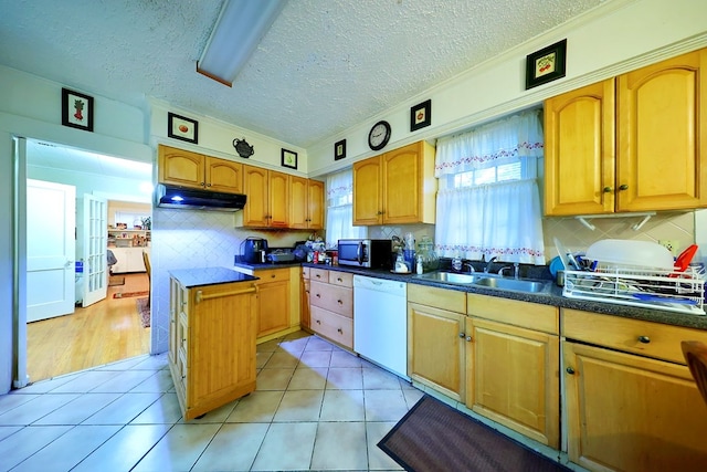 kitchen featuring light tile patterned floors, dishwasher, dark countertops, stainless steel microwave, and under cabinet range hood