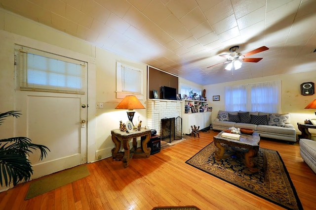 living area featuring a brick fireplace, ceiling fan, and wood finished floors