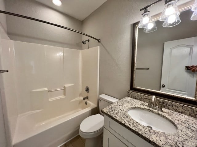 full bathroom with toilet, tile patterned flooring, a textured wall, vanity, and tub / shower combination