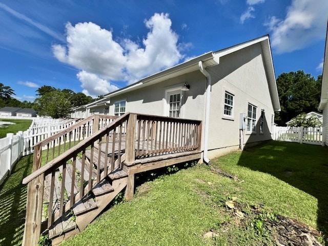 rear view of house featuring stucco siding, a wooden deck, a yard, and a fenced backyard