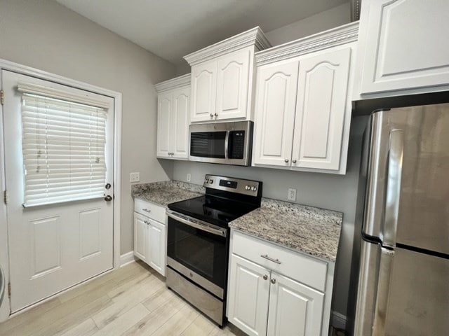 kitchen featuring white cabinets, light wood-type flooring, light stone countertops, baseboards, and appliances with stainless steel finishes