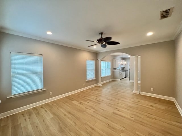 spare room with visible vents, ornamental molding, arched walkways, baseboards, and ceiling fan with notable chandelier