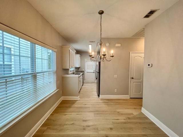 unfurnished dining area featuring baseboards, a chandelier, visible vents, and light wood-style floors