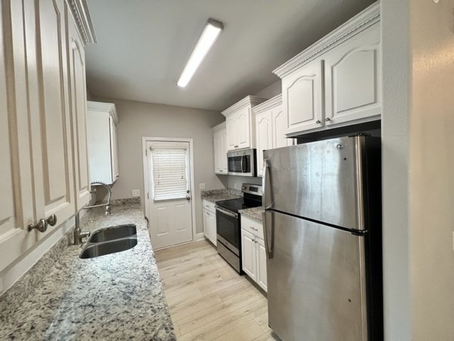 kitchen featuring a sink, light wood-style floors, white cabinetry, appliances with stainless steel finishes, and light stone countertops