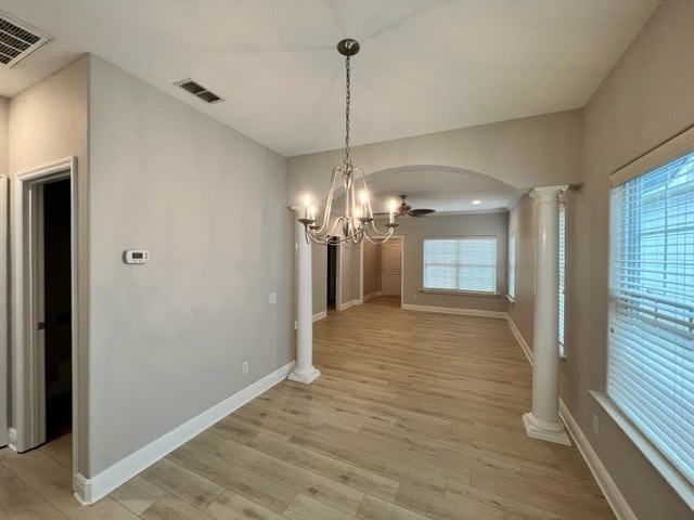 unfurnished dining area featuring arched walkways, plenty of natural light, visible vents, and ornate columns