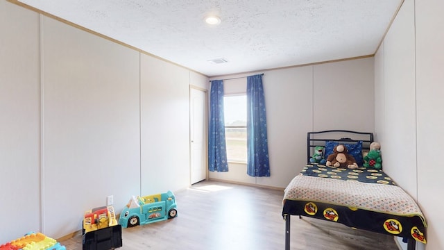 bedroom with crown molding, a textured ceiling, visible vents, and wood finished floors