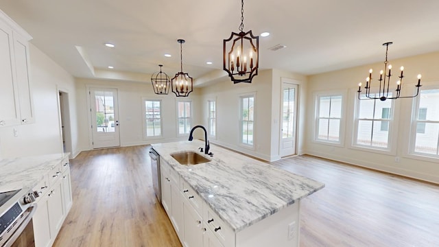 kitchen with white cabinetry, sink, a center island with sink, and decorative light fixtures