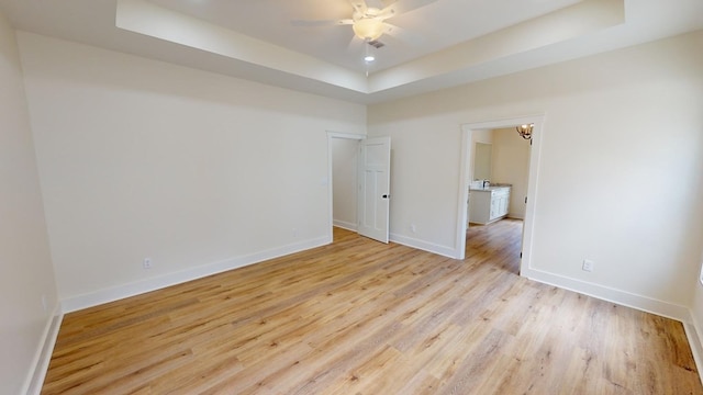 empty room with a raised ceiling, ceiling fan, and light wood-type flooring