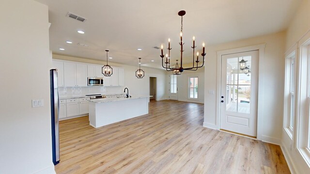 kitchen featuring tasteful backsplash, hanging light fixtures, an island with sink, light hardwood / wood-style floors, and white cabinets