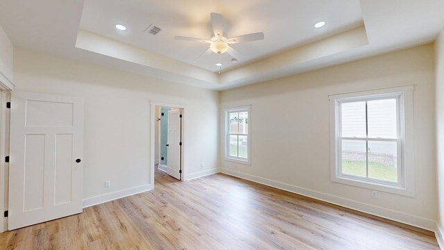 unfurnished bedroom featuring a tray ceiling and light wood-type flooring