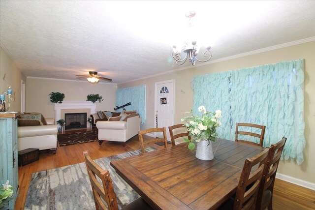 dining space with hardwood / wood-style flooring, ornamental molding, ceiling fan with notable chandelier, and a textured ceiling