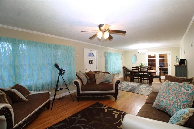 living room featuring hardwood / wood-style flooring, crown molding, ceiling fan with notable chandelier, and a textured ceiling